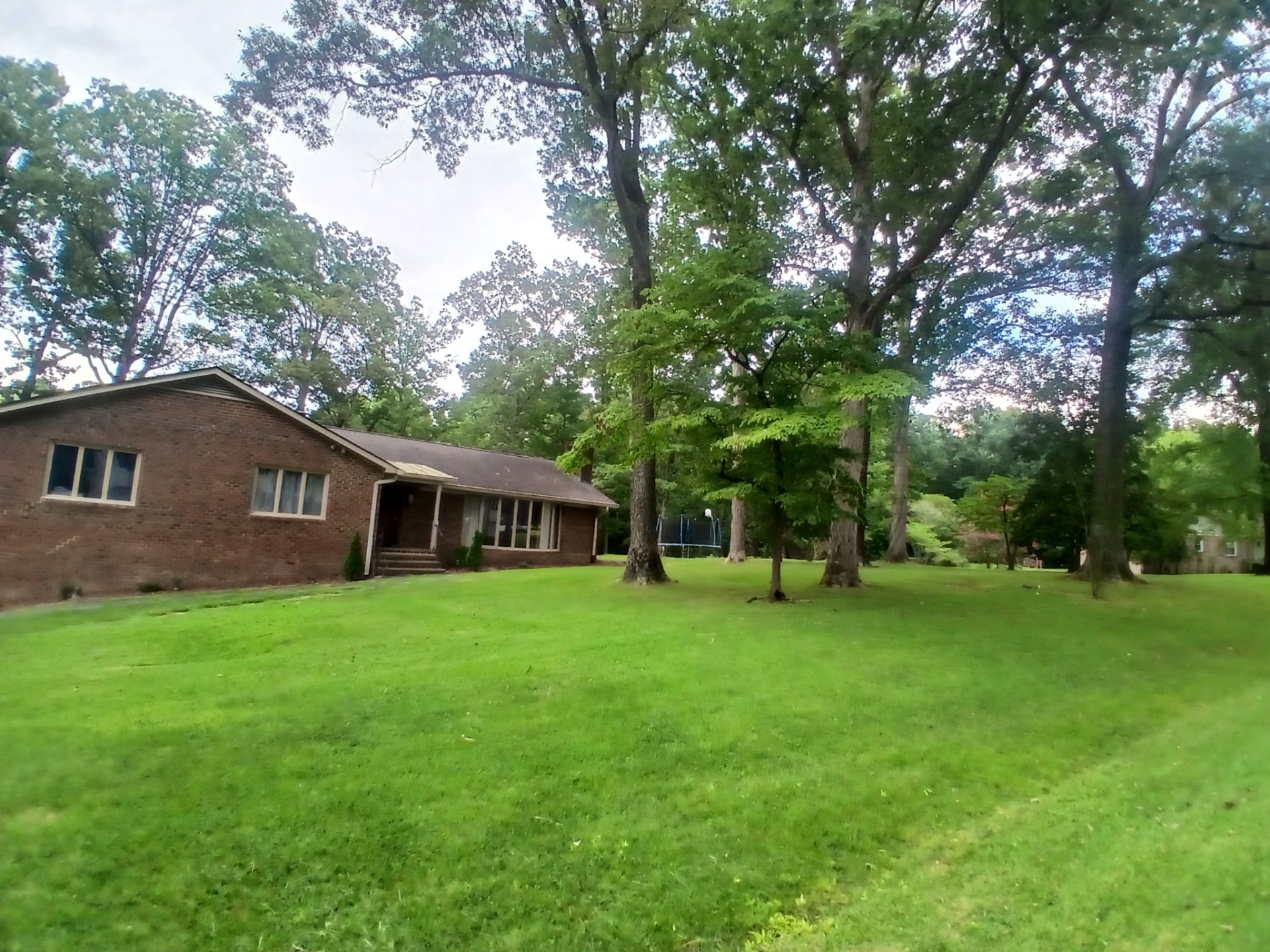 Full lawn mowing and trimming around a shaded brick home in Petersburg, VA — Basnight Enterprises, LLC.